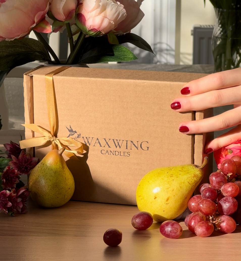Waxwing candles box with flowers, pears, and grapes on a wooden surface