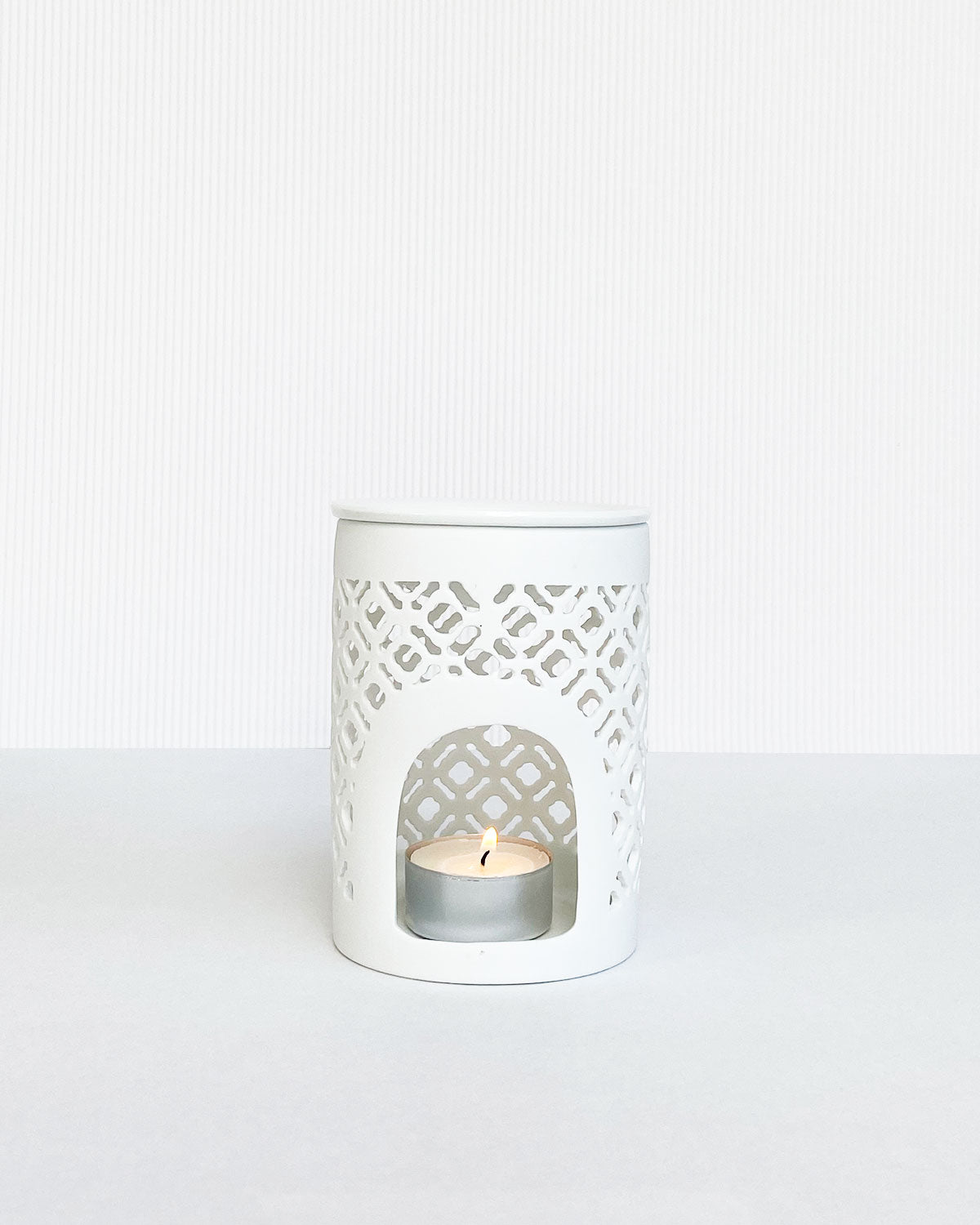 Matt white lattice cut wax burner with lit tea light inside.